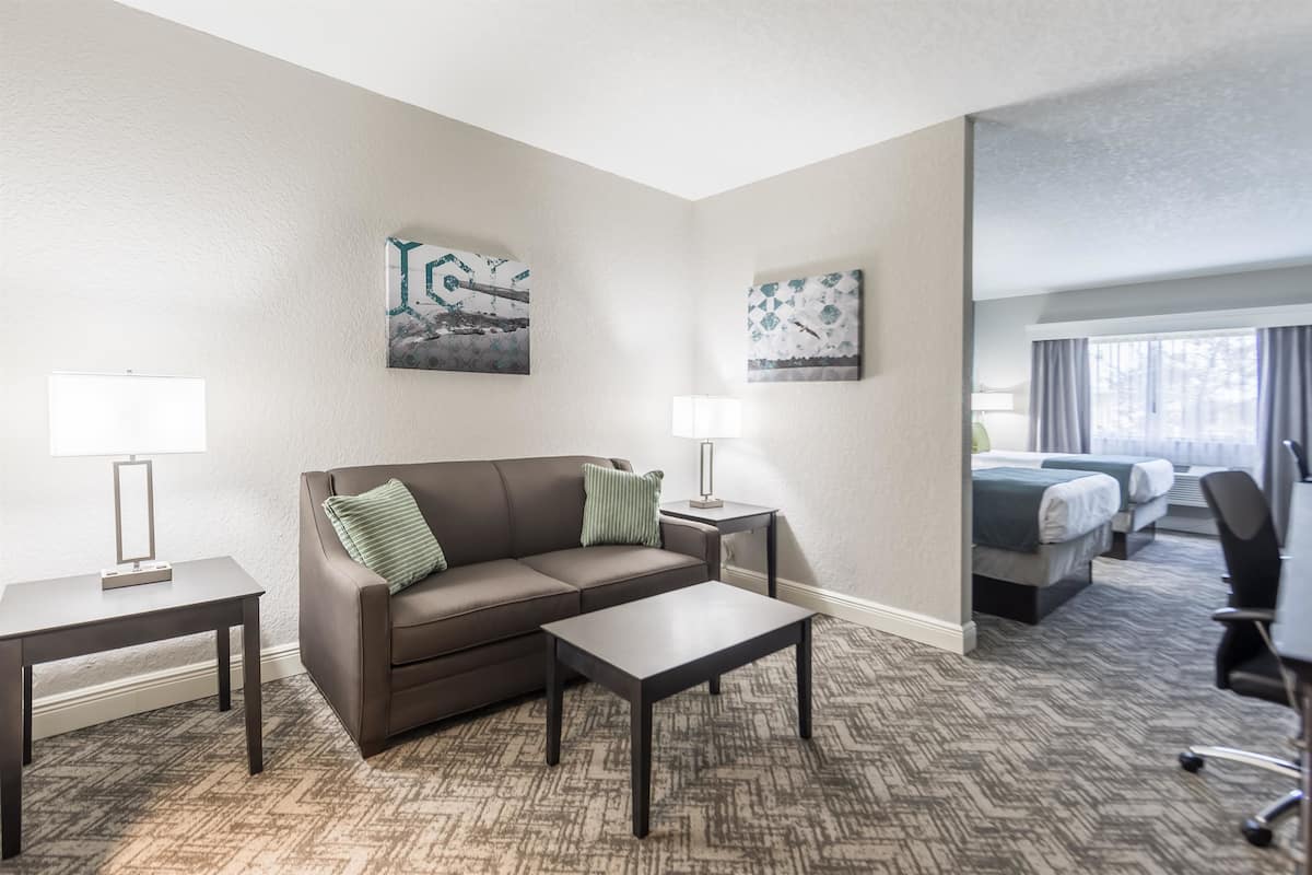 A hotel room with a brown leather sofa, a small table, two wall-mounted lamps, and a bed with a gray headboard.