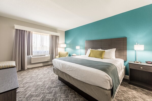 Une chambre d’hôtel avec un grand lit, une table de chevet, une lampe, une chaise et une fenêtre avec des rideaux.