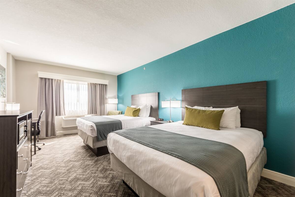 A hotel room with two beds, a desk, and a window with curtains.