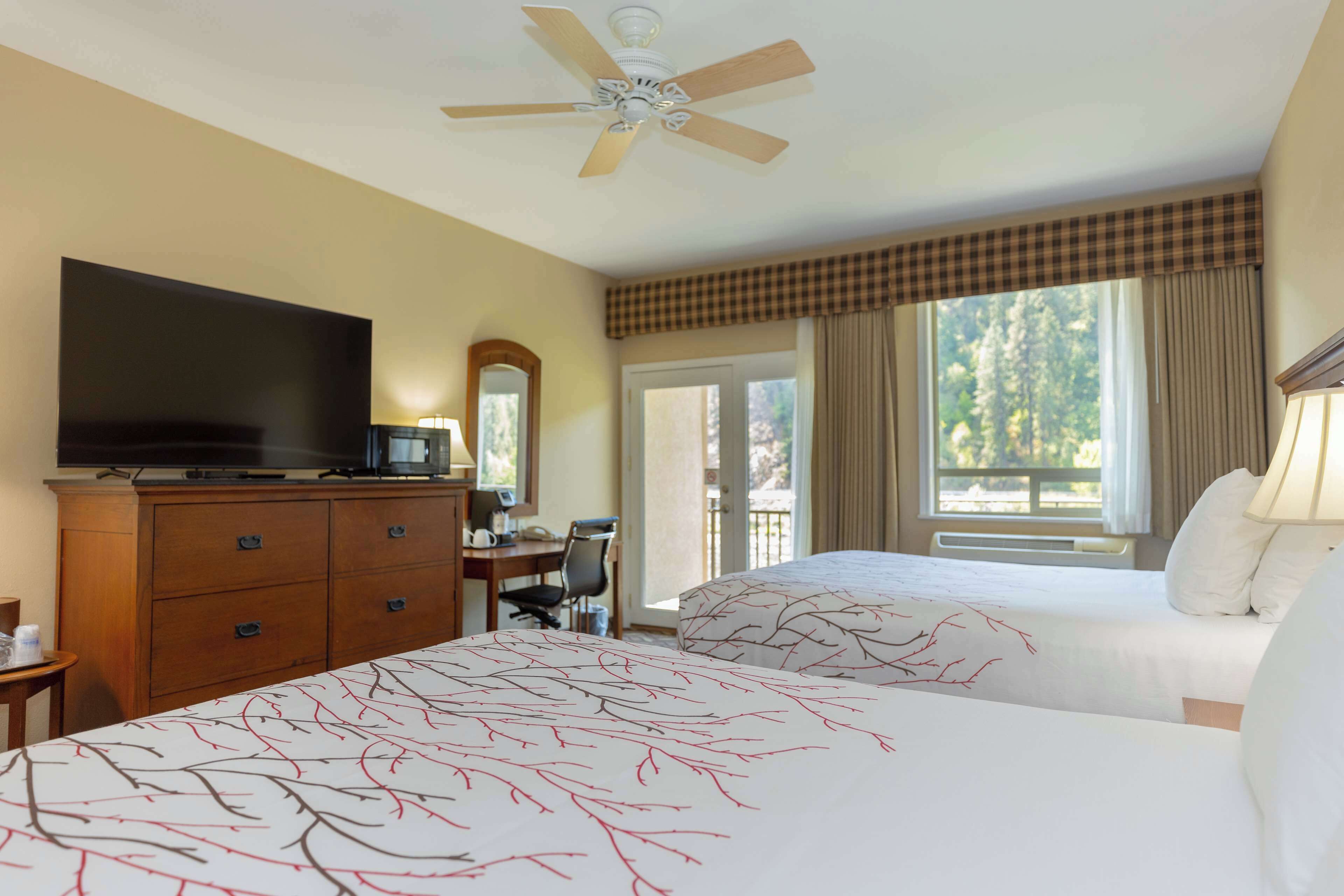 A hotel room with two beds, a television, a desk with a chair, and a large window with curtains.