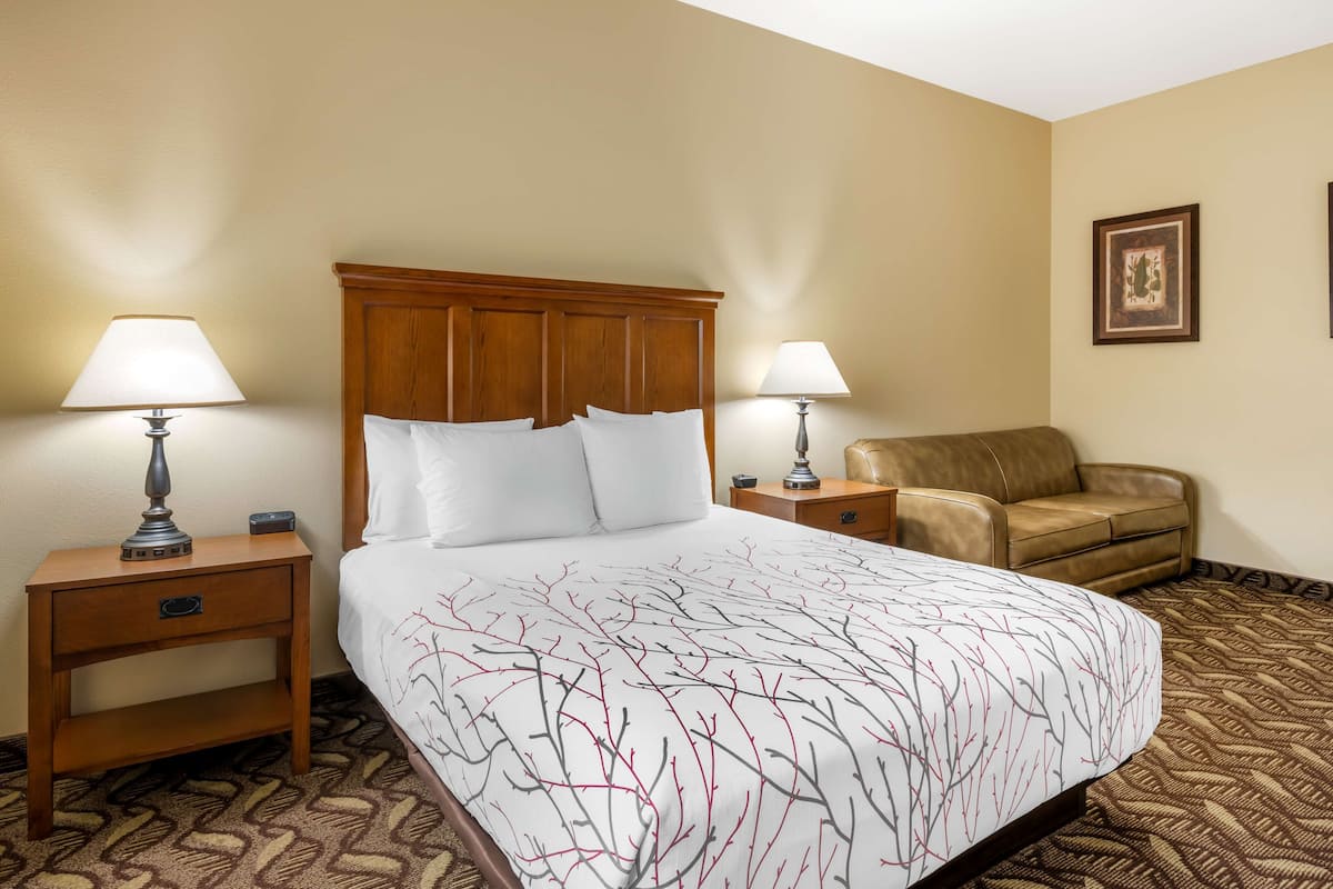 A hotel room with a large bed, two bedside tables with lamps, a brown leather armchair, and a patterned carpet.