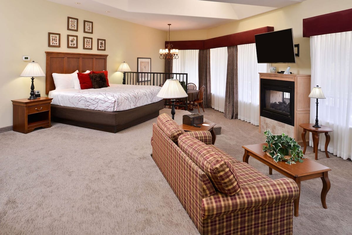 A hotel room with a bed, a sofa, a TV, a fireplace, and a dining area.