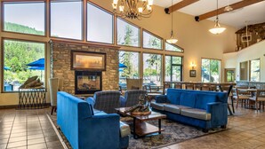 A spacious living area with large windows, a stone fireplace, blue sofas, and a dining area. - Best Western Lodge At River's Edge (Orofino)