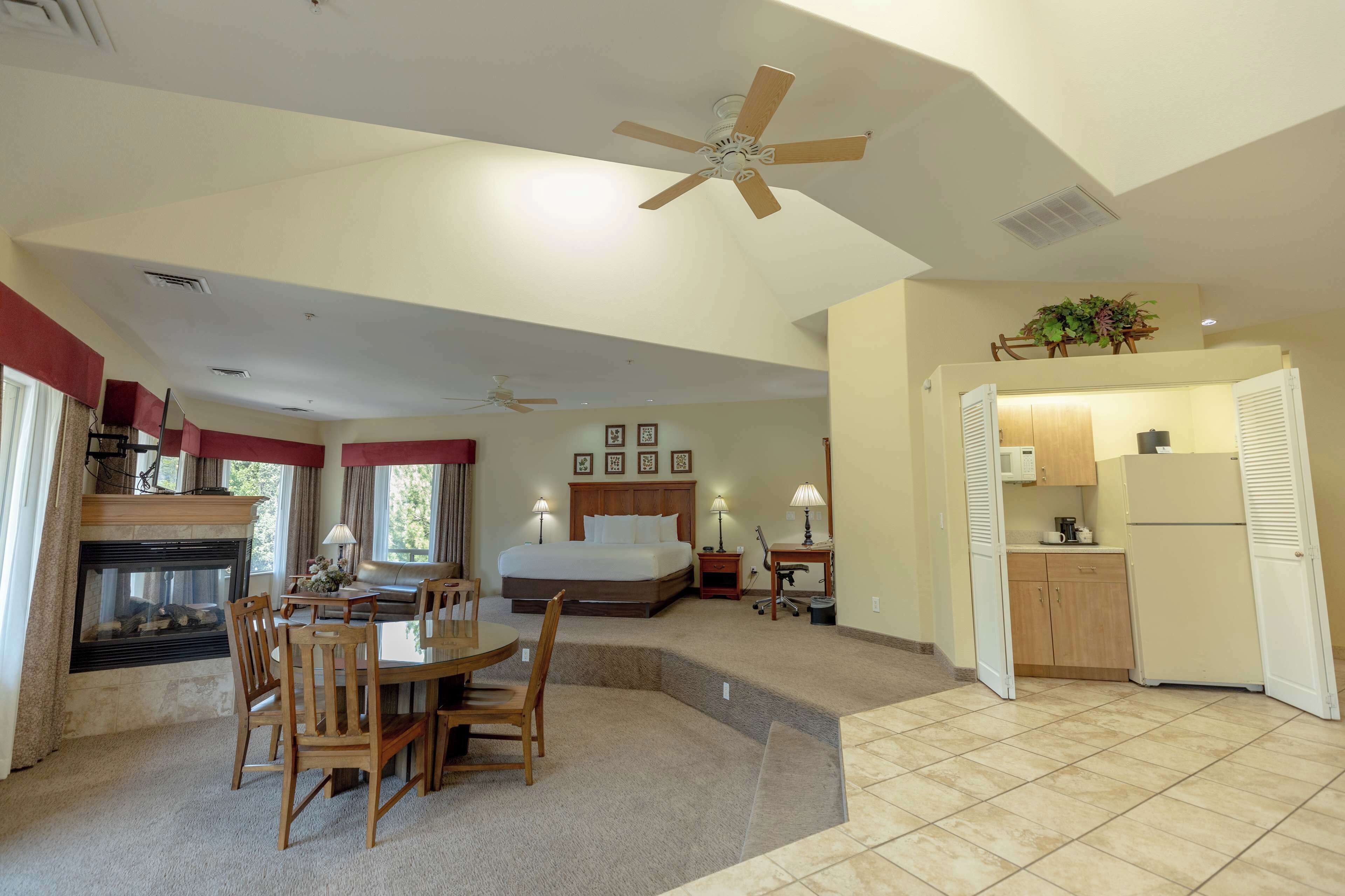 A hotel room with a bed, a dining table with chairs, a kitchen area, and a ceiling fan.