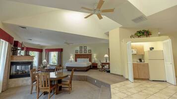 A hotel room with a bed, a dining table with chairs, a kitchen area, and a ceiling fan.