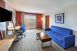 A modern living room with a blue sofa, a desk with a computer, a television, and a lamp.