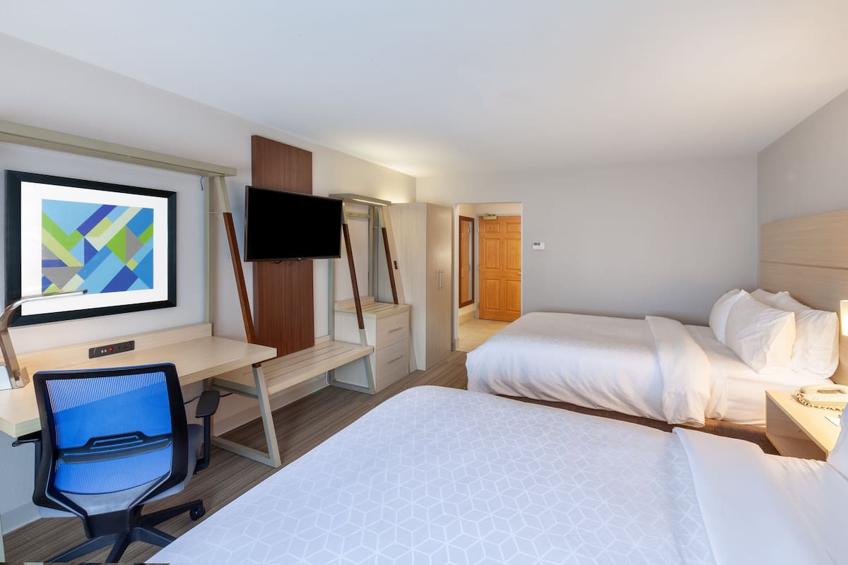 A hotel room with two beds, a desk with a chair, a TV, and a painting on the wall.