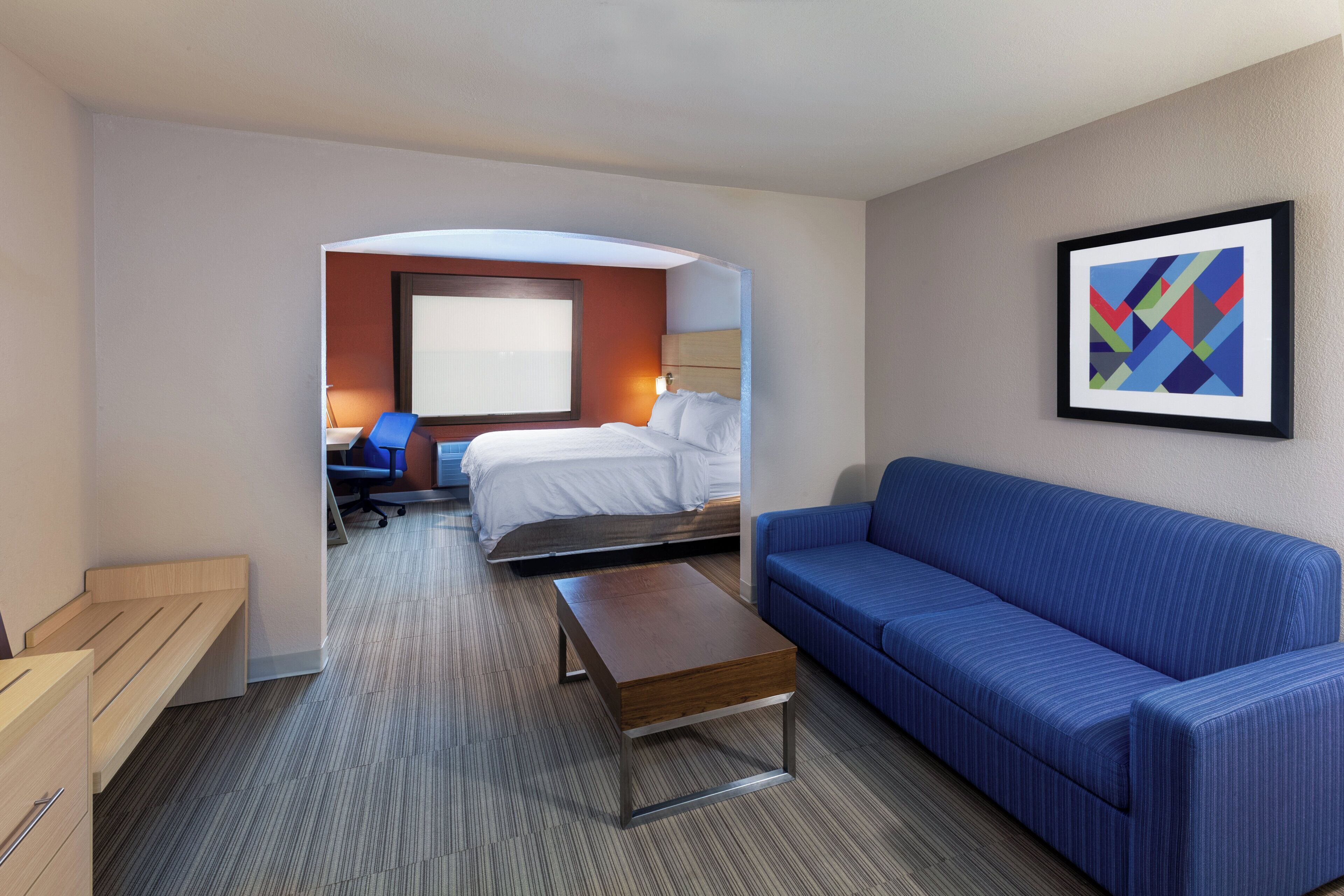 Ein Hotelzimmer mit einem Bett, einem blauen Sofa, einer Holzbank, einem Schreibtisch und einem Stuhl.