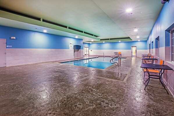 An indoor swimming pool with a blue and white wall, a concrete floor, and a seating area with tables and chairs. - Holiday Inn Express Hotel & Suites Jenks by IHG (Jenks)