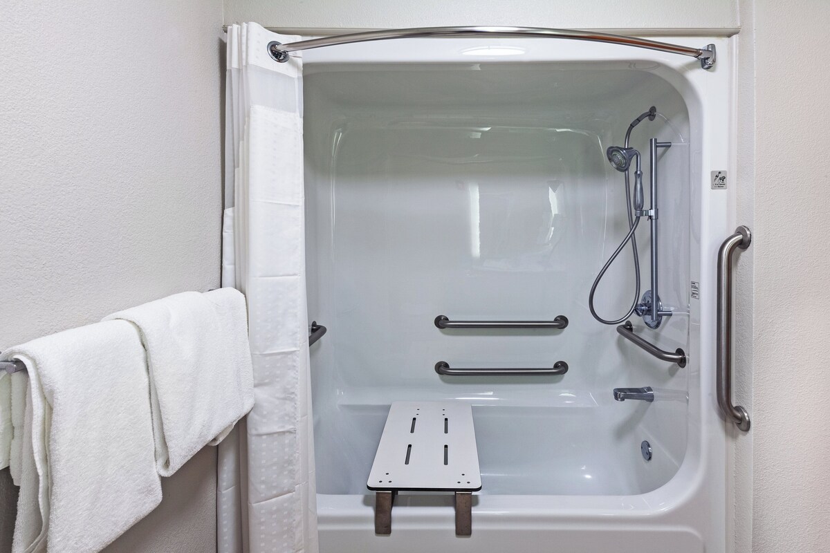 A white bathtub with a shower head, grab bars, and a small step stool.