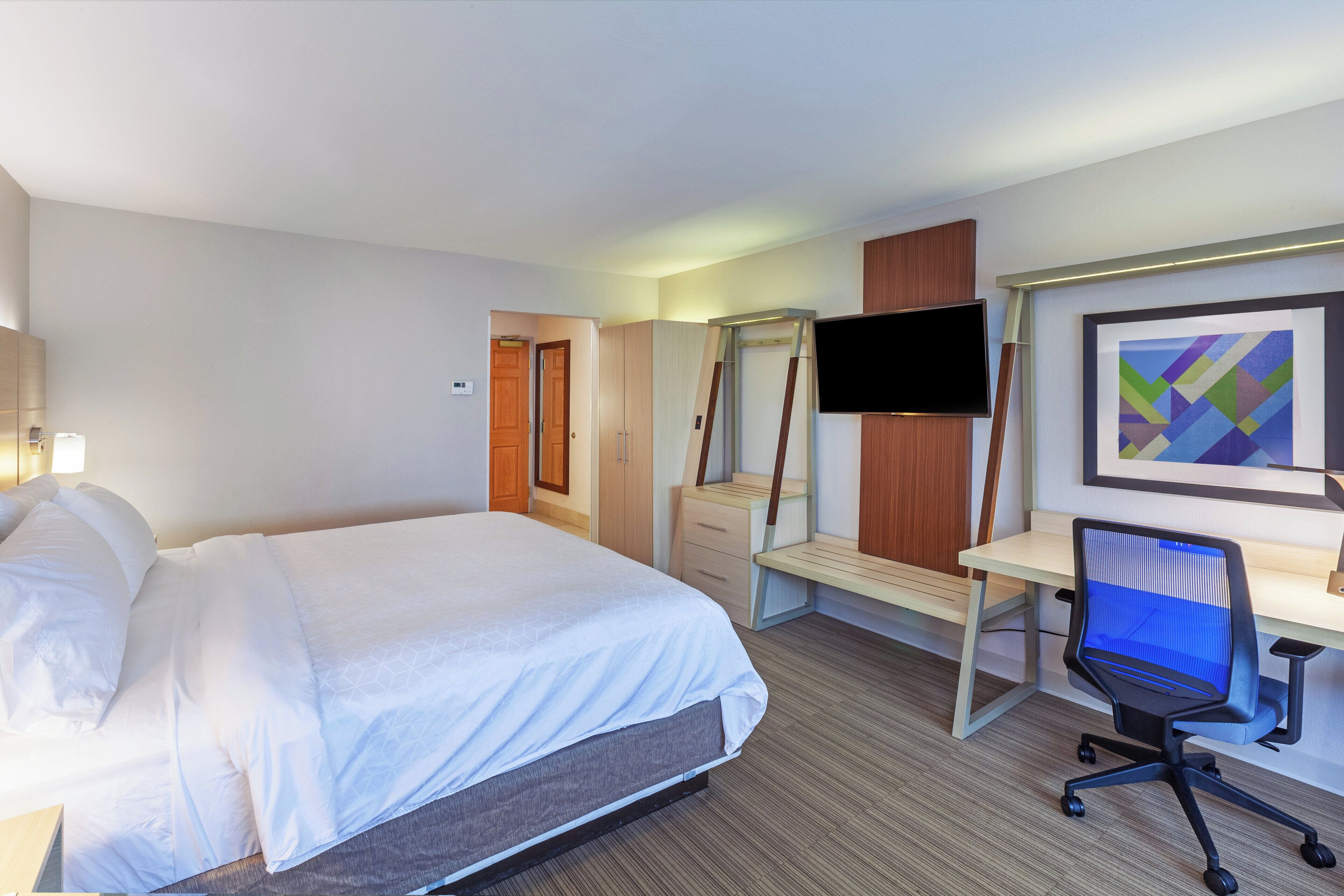 Habitación de hotel con cama, escritorio, silla, televisor y una obra de arte en la pared.