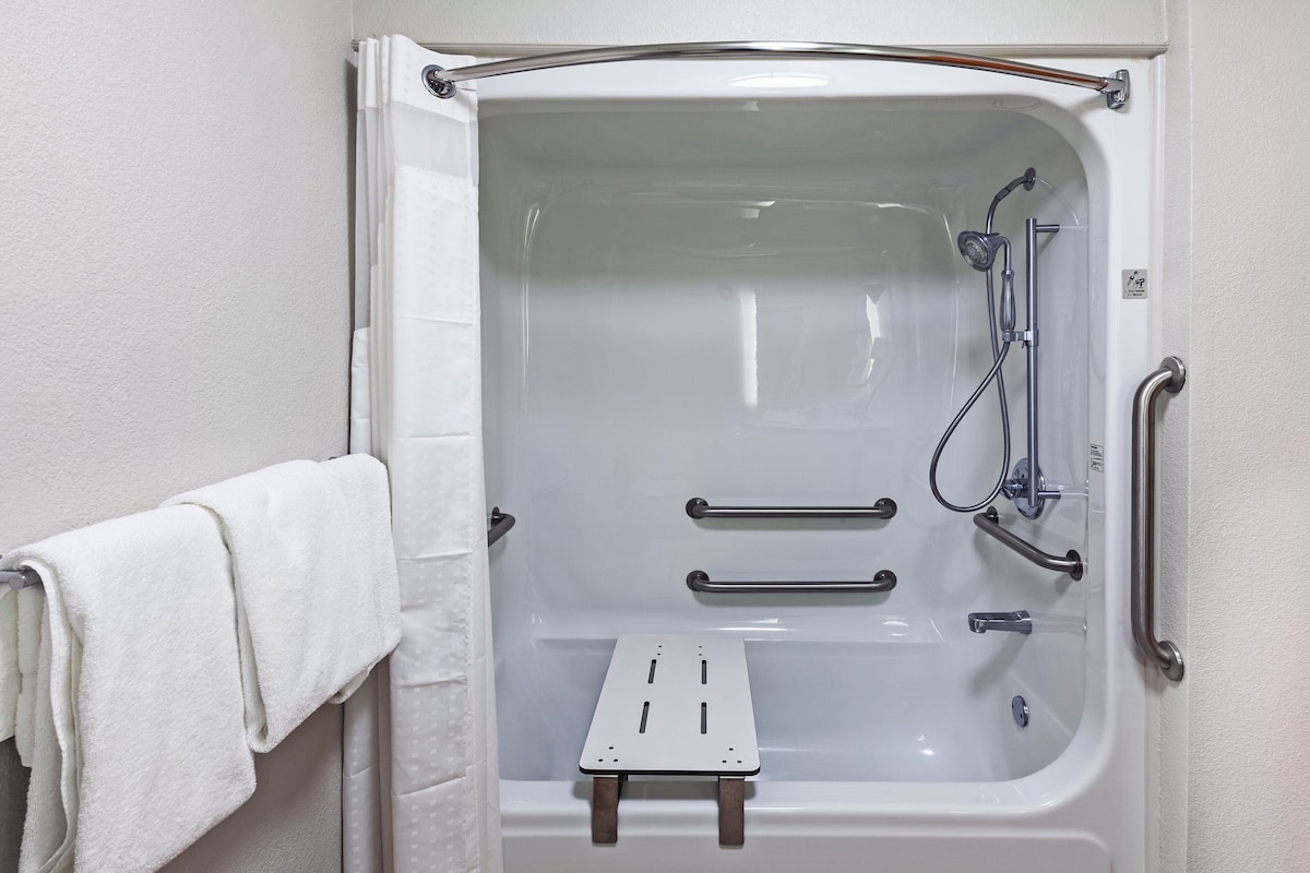 A white bathtub with grab bars, a shower head, and a handheld shower attachment.