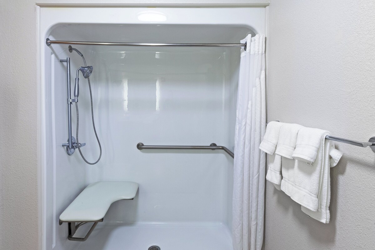 A walk-in shower with a grab bar, a bench, and a towel rack.