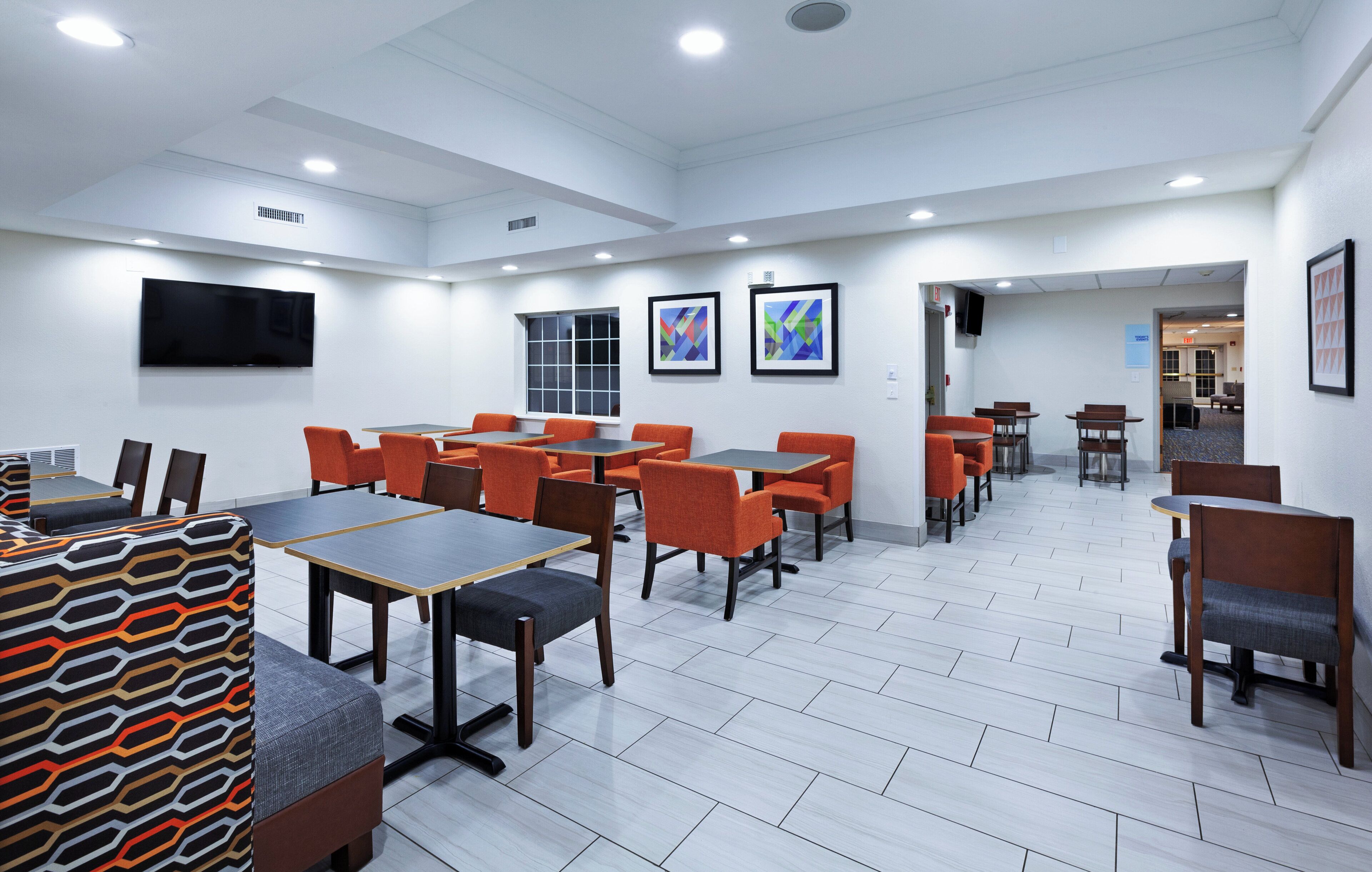 A conference room with tables and chairs, a flat-screen TV, and framed artwork on the walls.