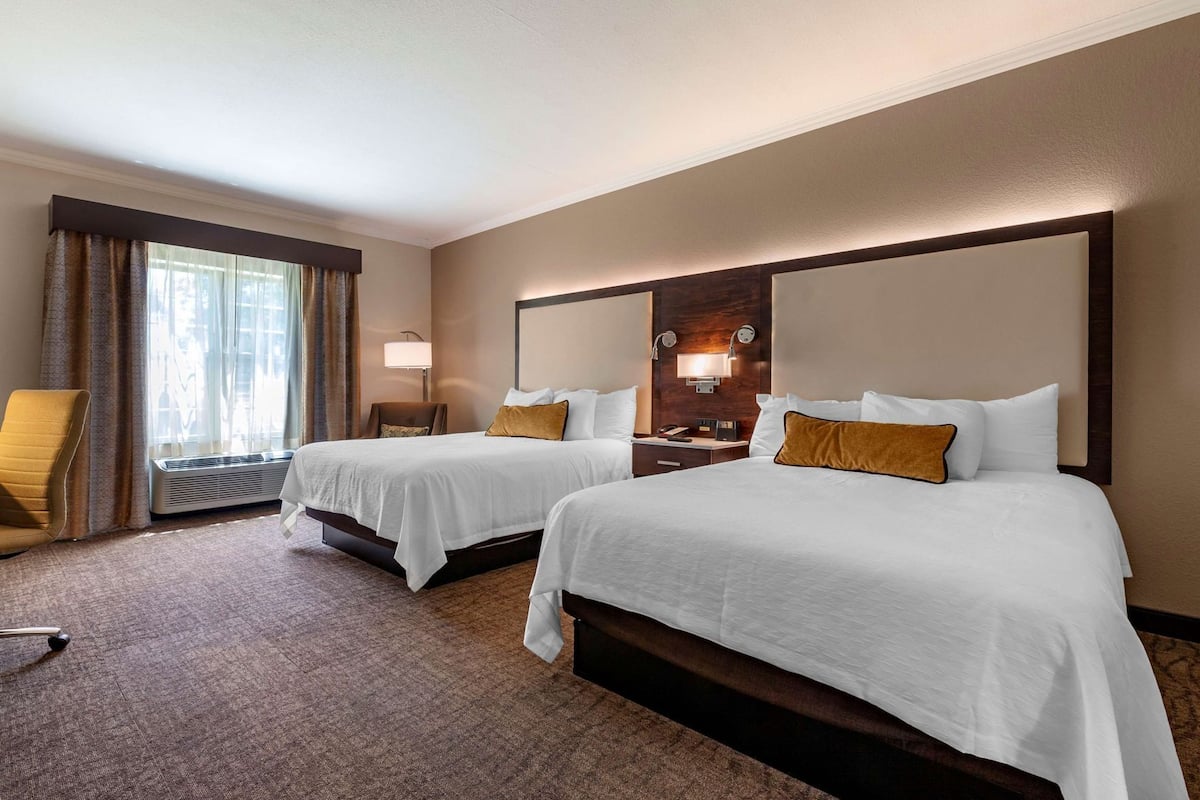 A hotel room with two beds, a chair, a desk, and a window with curtains.