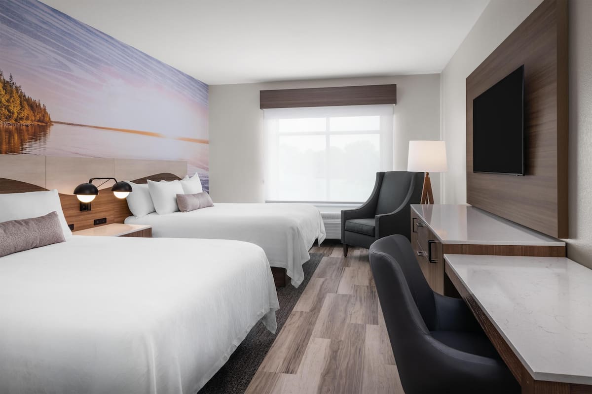 A hotel room with two beds, a desk, a chair, a TV, and a large window.