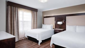 A hotel room with two beds, a wooden floor, a large window with curtains, and a wall-mounted light fixture.