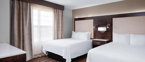 Une chambre d’hôtel avec deux lits, un plancher en bois, une grande fenêtre avec des rideaux et un luminaire fixé au mur.