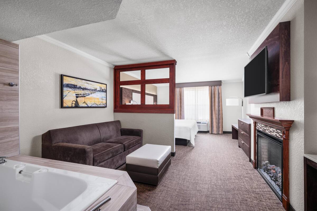 A hotel room with a large bed, a sofa, a TV, a fireplace, and a painting on the wall.