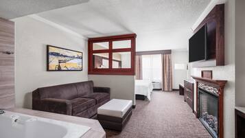 A hotel room with a large bed, a sofa, a TV, a fireplace, and a painting on the wall.
