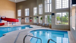 An indoor swimming pool with a red slide, large windows, and lounge chairs.