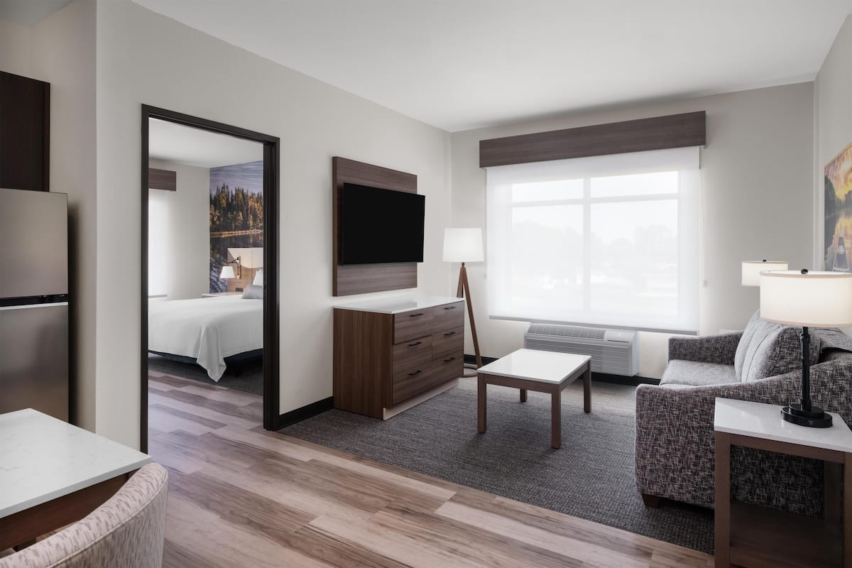 A hotel room with a bed, a desk, a chair, a sofa, a TV, and a window.