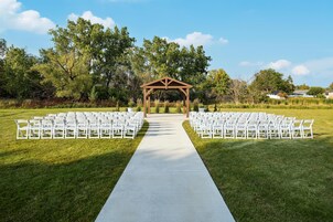 Montaje de ceremonia de boda con un pasillo blanco, sillas blancas a cada lado y un arco de madera.