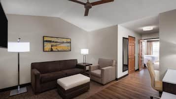 Una habitación de hotel moderna con un sofá marrón, un sillón pequeño, un escritorio y un ventilador de techo.
