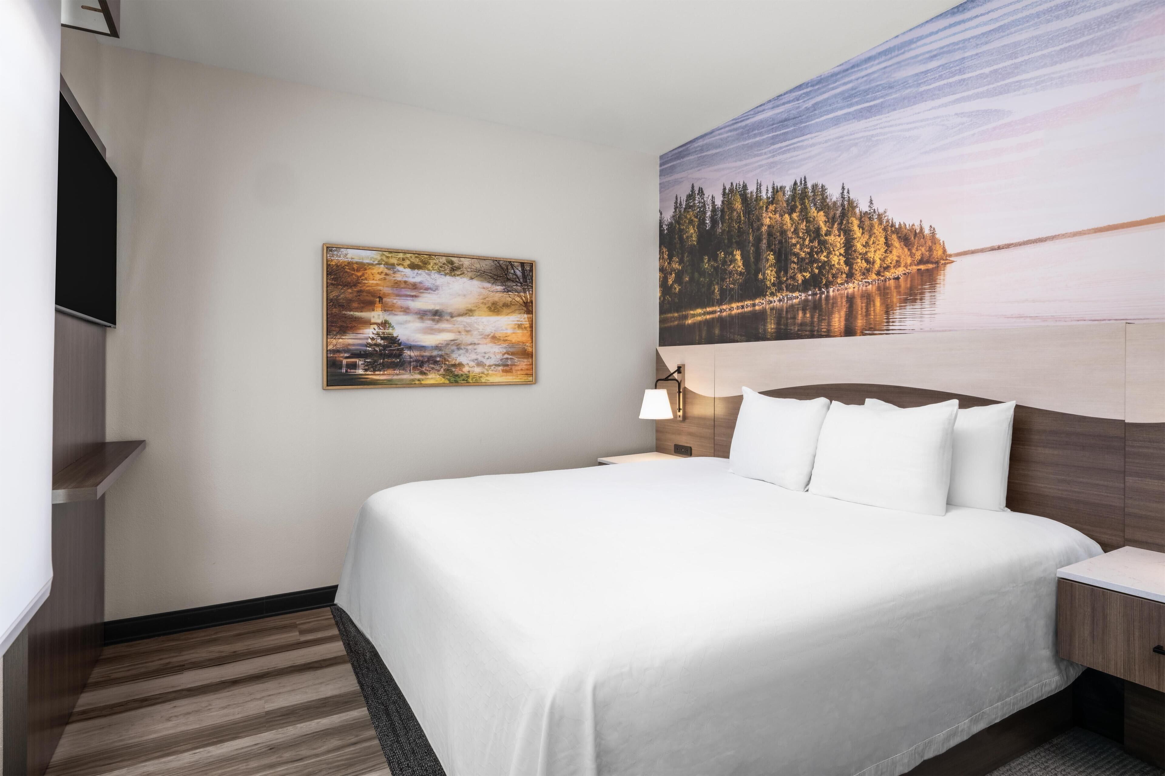 A hotel room with a large bed, a nightstand, a lamp, and two paintings on the wall.