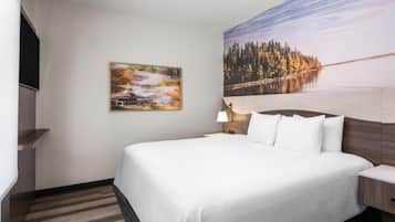 A hotel room with a large bed, a nightstand, a lamp, and two paintings on the wall.