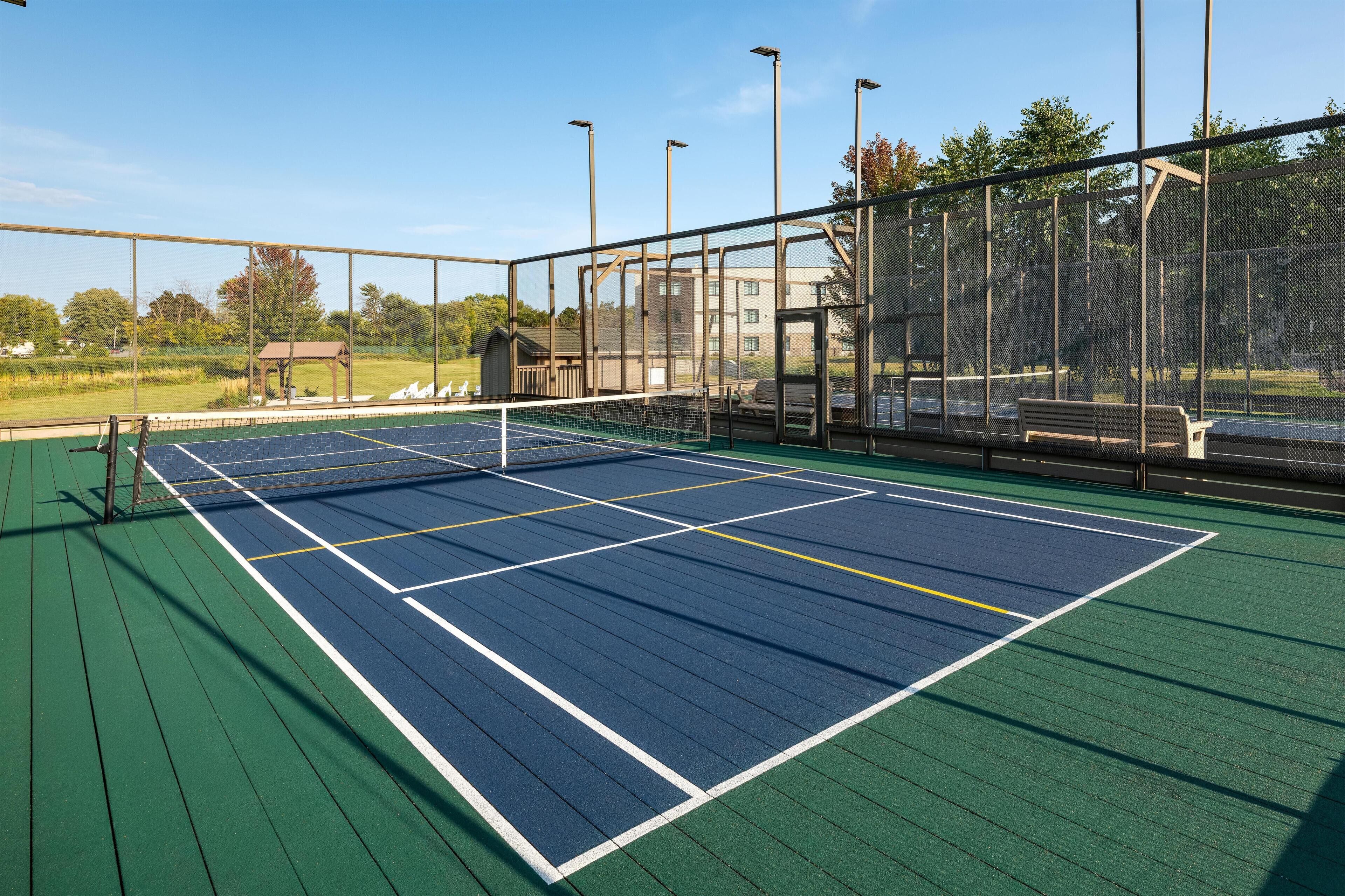 Una cancha de tenis al aire libre con red, rodeada por una valla y un banco.