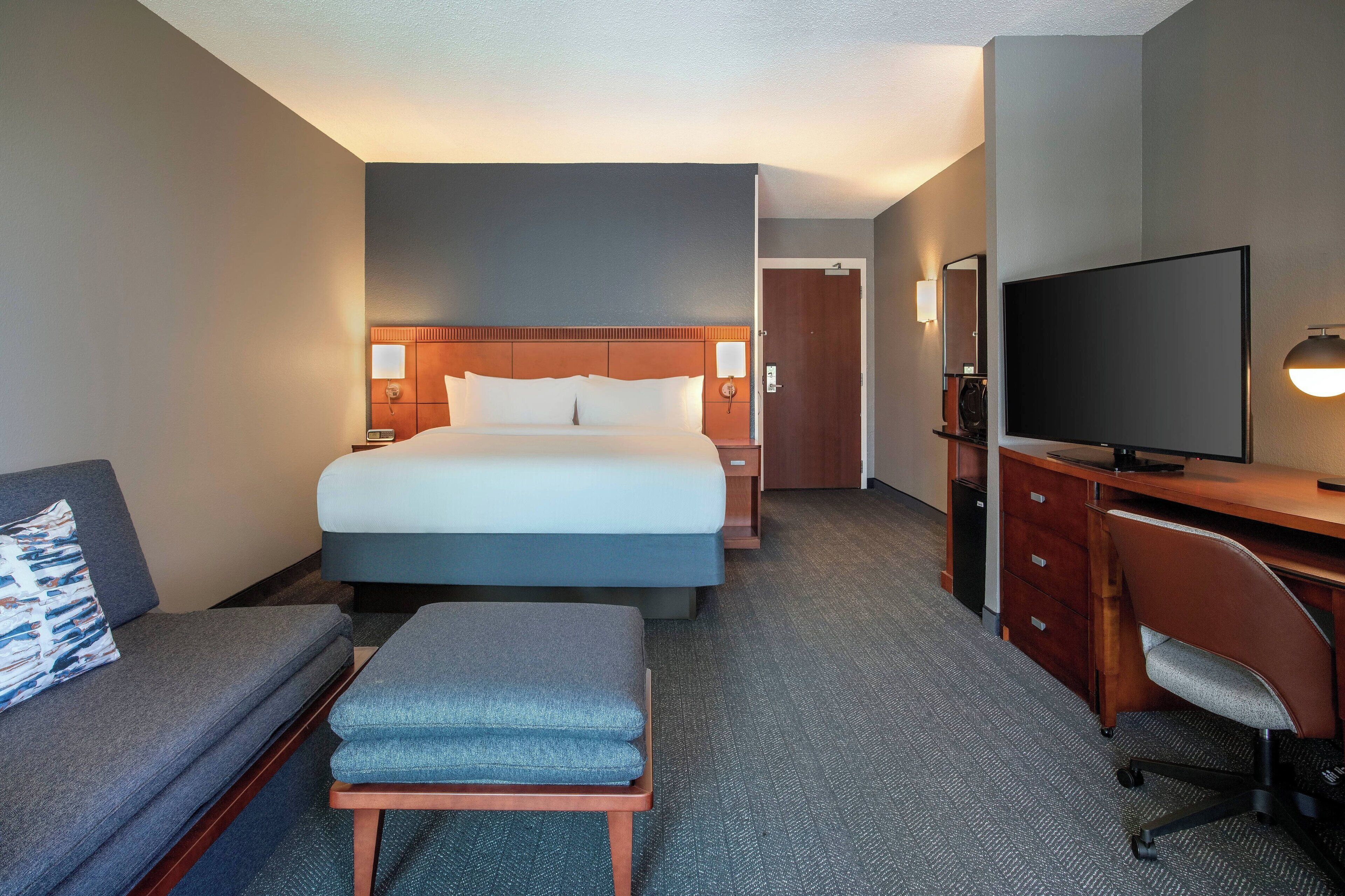 Habitación de hotel con cama, escritorio, televisión, sofá y una mesita.