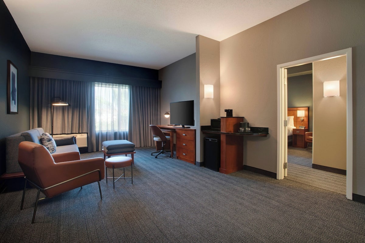 A hotel room with a sofa, armchair, desk, and television.