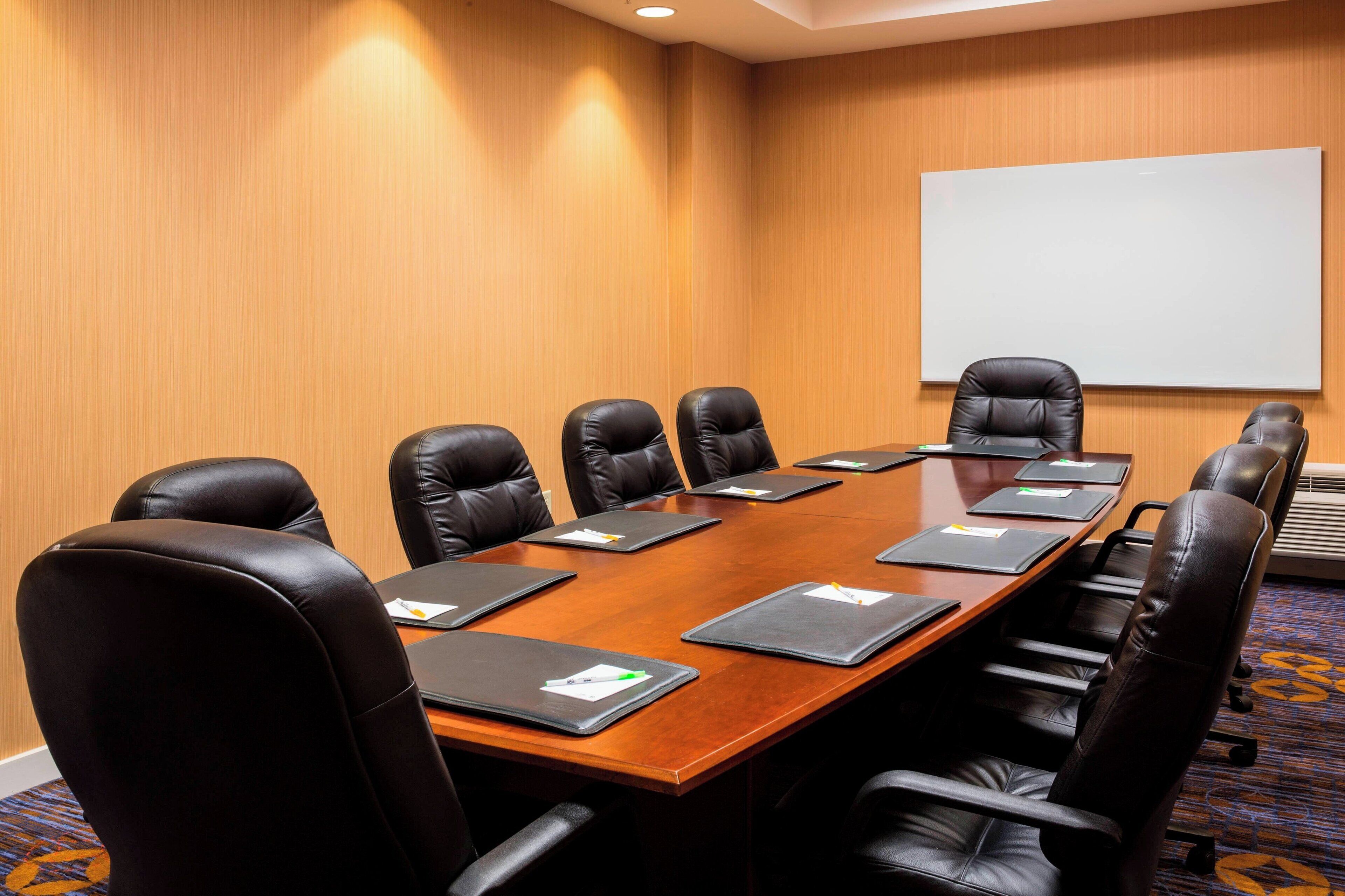 A conference room with a wooden table, black leather chairs, and a whiteboard on the wall.