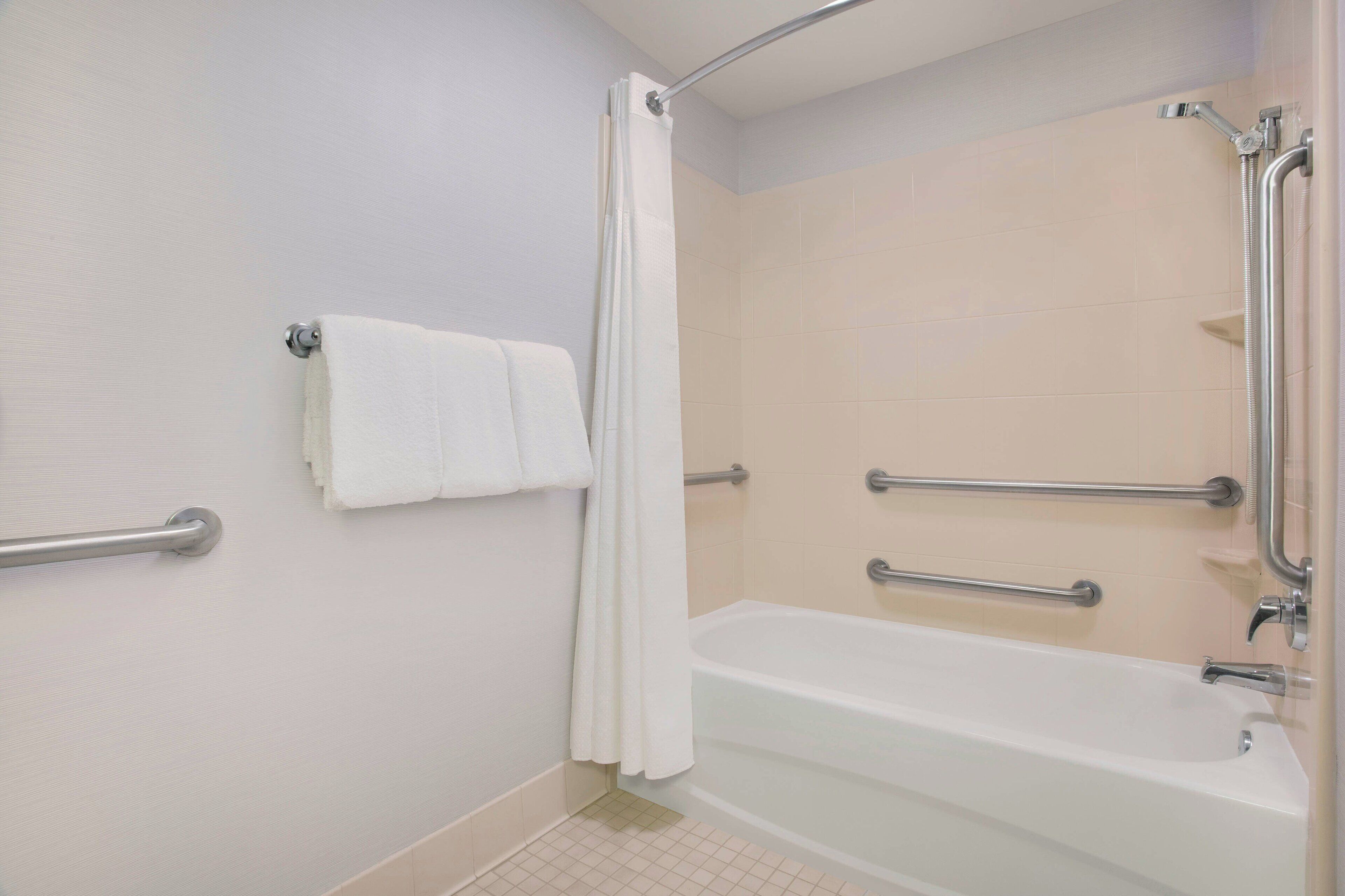A bathroom with a bathtub, a shower curtain, and grab bars.