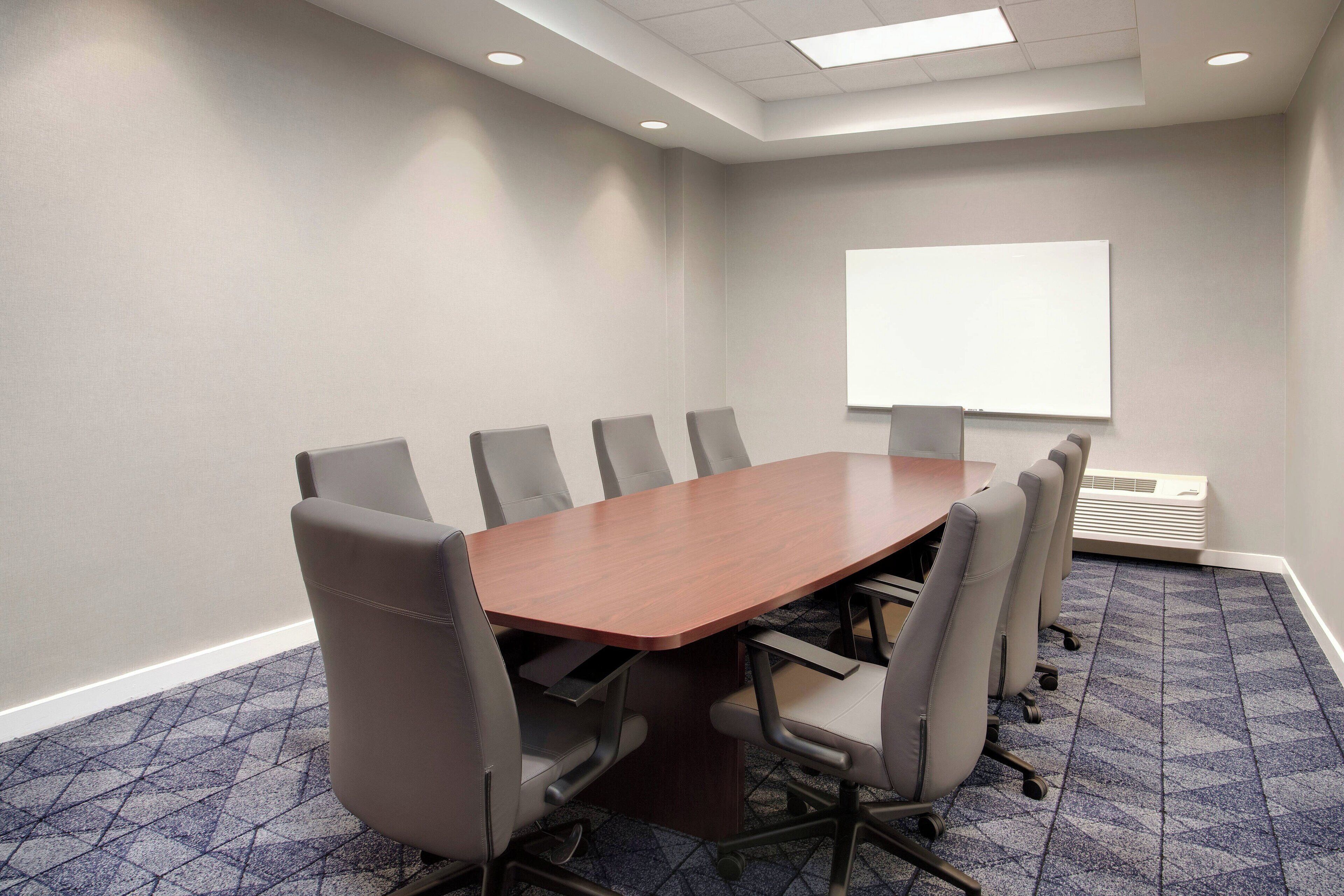 A conference room with a large table, six chairs, a whiteboard, and a carpeted floor.