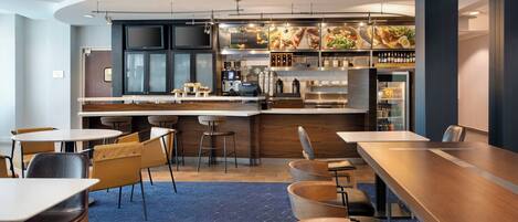 A modern bar area with seating and a counter, featuring a menu display and various beverages.