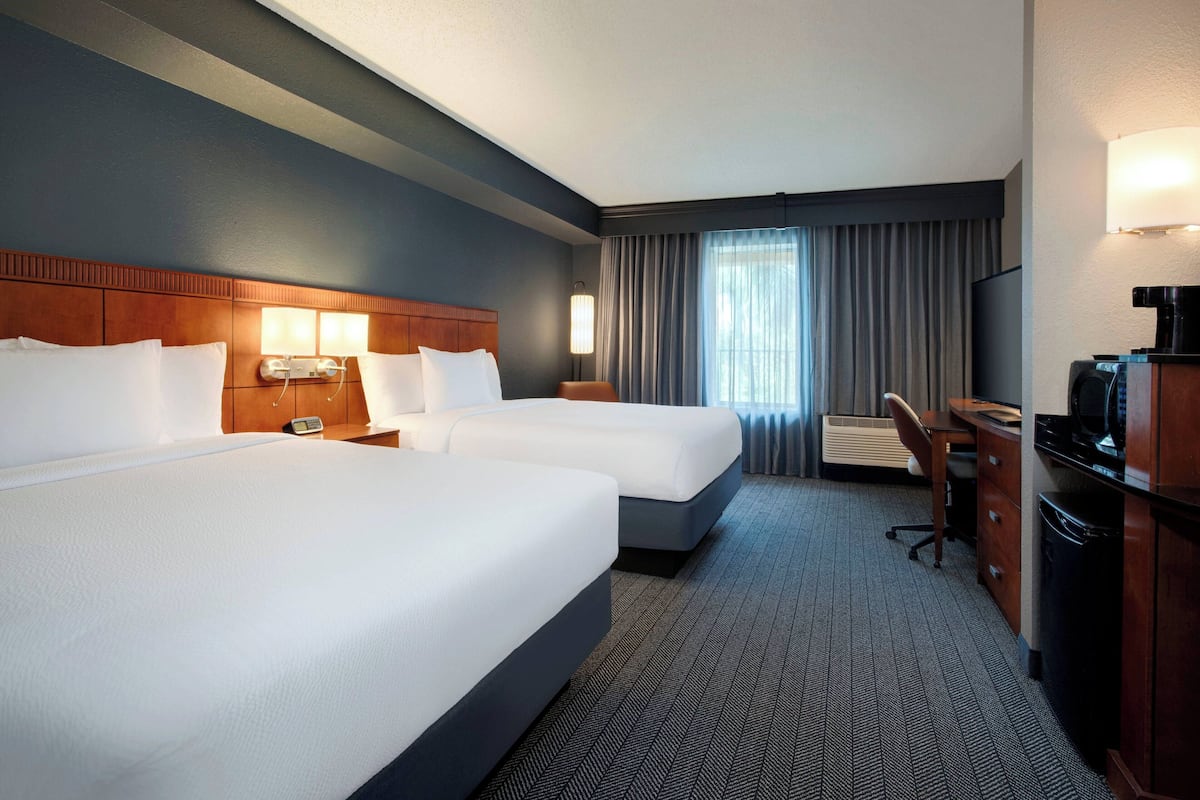 A hotel room with two beds, a desk, a chair, a television, and a coffee machine.