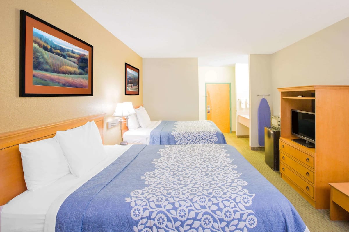 A hotel room with two beds, a TV, a dresser, and framed pictures on the wall.