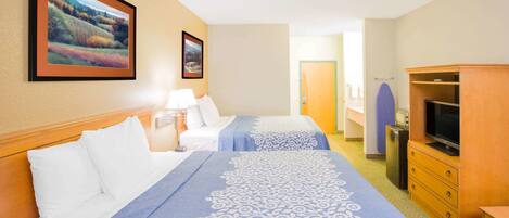 Habitación de hotel con dos camas, televisor, cómoda y cuadros en la pared.