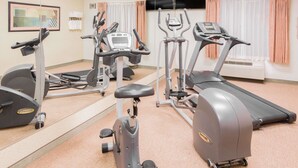Un gimnasio con máquinas de cardio, un espejo grande y un televisor en la pared.