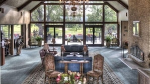 A spacious room with a high ceiling and exposed wooden beams, a large chandelier, and a view of the outdoors through large windows. - Maddens On Gull Lake (Brainerd)