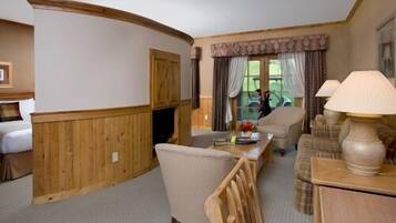 A cozy hotel room with a wooden accent wall, a dining area with a table and chairs, a sofa, and a lamp.
