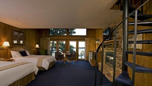 A room with two beds, a small table with chairs, a fireplace, and a view of trees through large windows. - Maddens On Gull Lake (Brainerd)