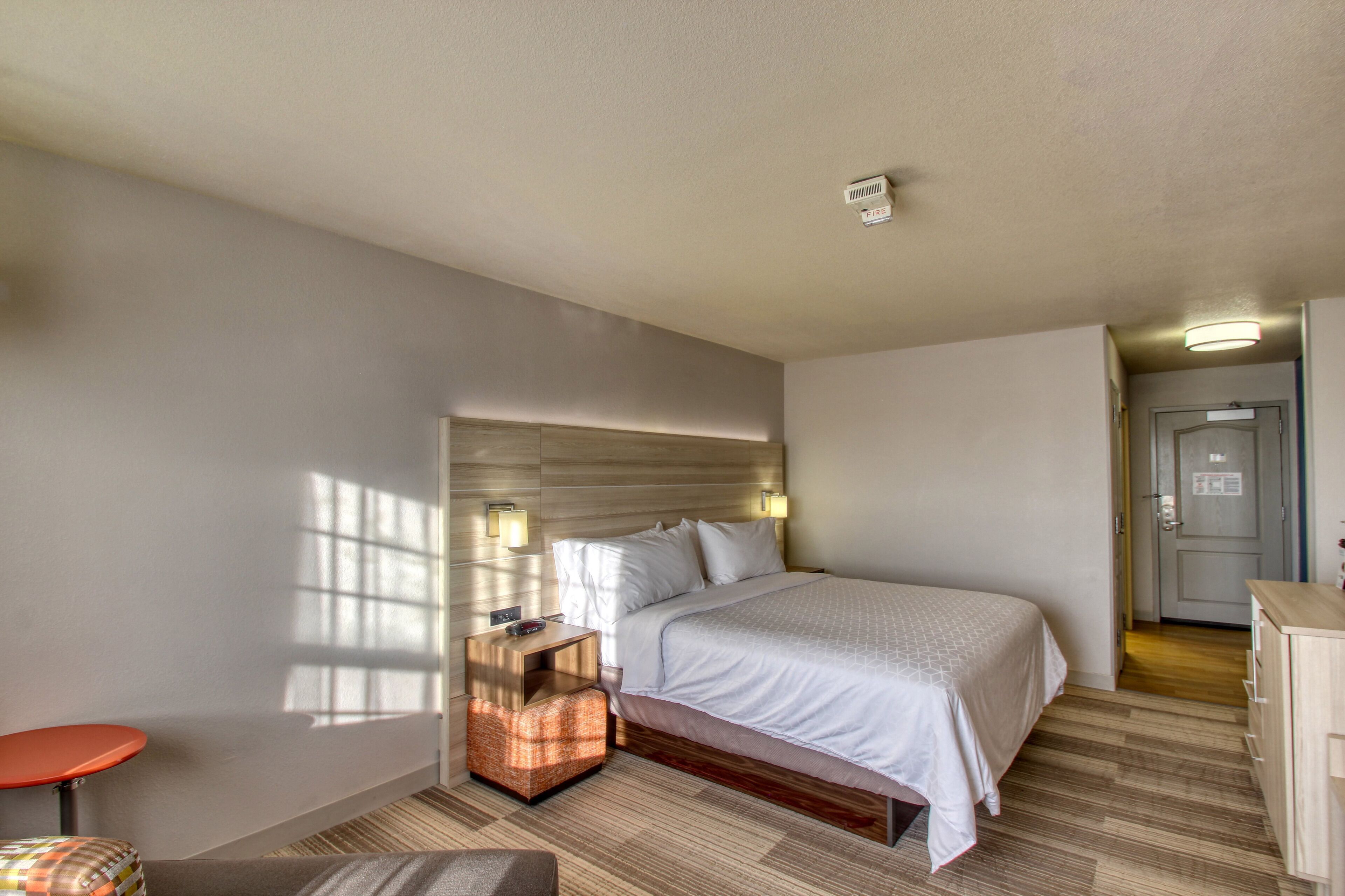 Habitación de hotel con cama, mesita de noche, una silla y una pequeña mesa.