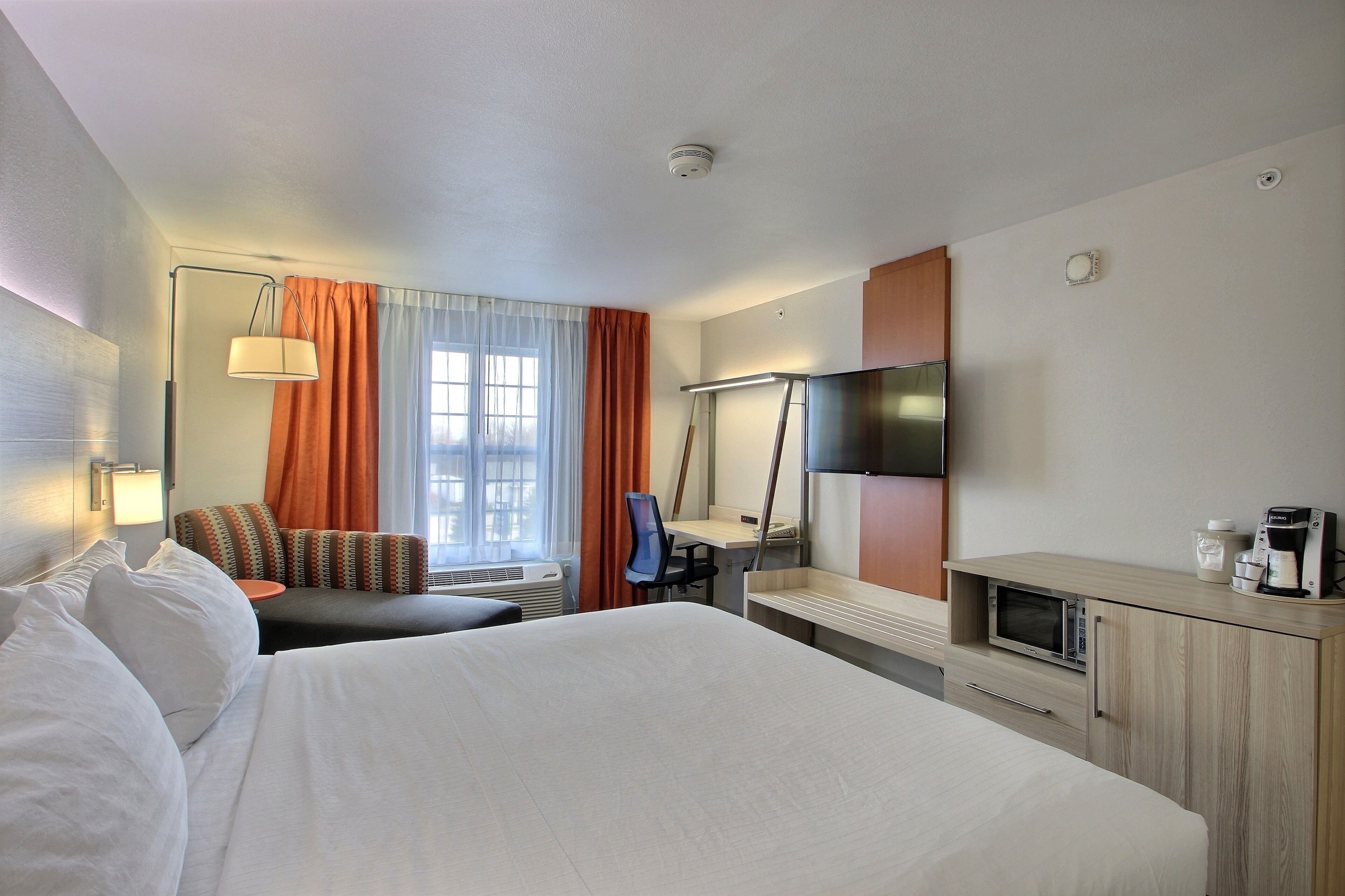 Ein Hotelzimmer mit einem großen Bett, einem Schreibtisch mit Computer, einem Fernseher und einer Mikrowelle.