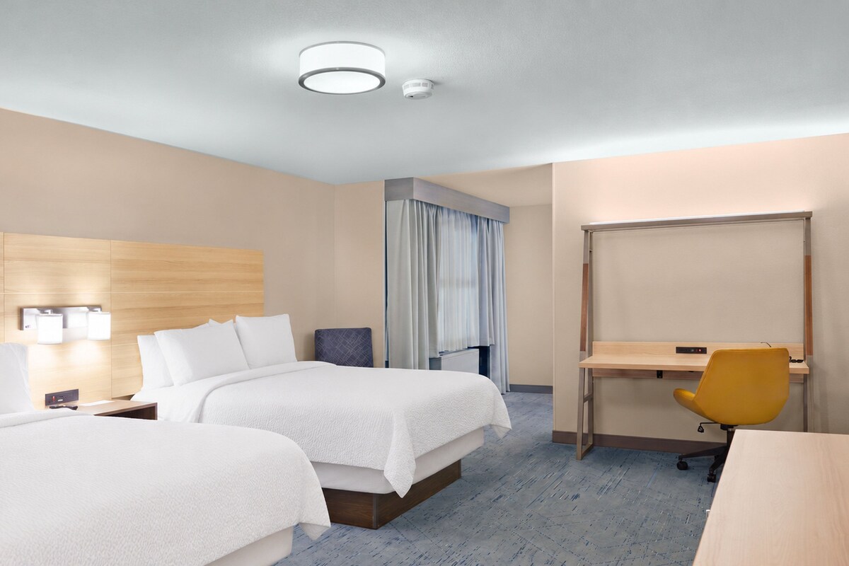 Una habitación de hotel con dos camas, un escritorio, una silla y una ventana con cortinas.