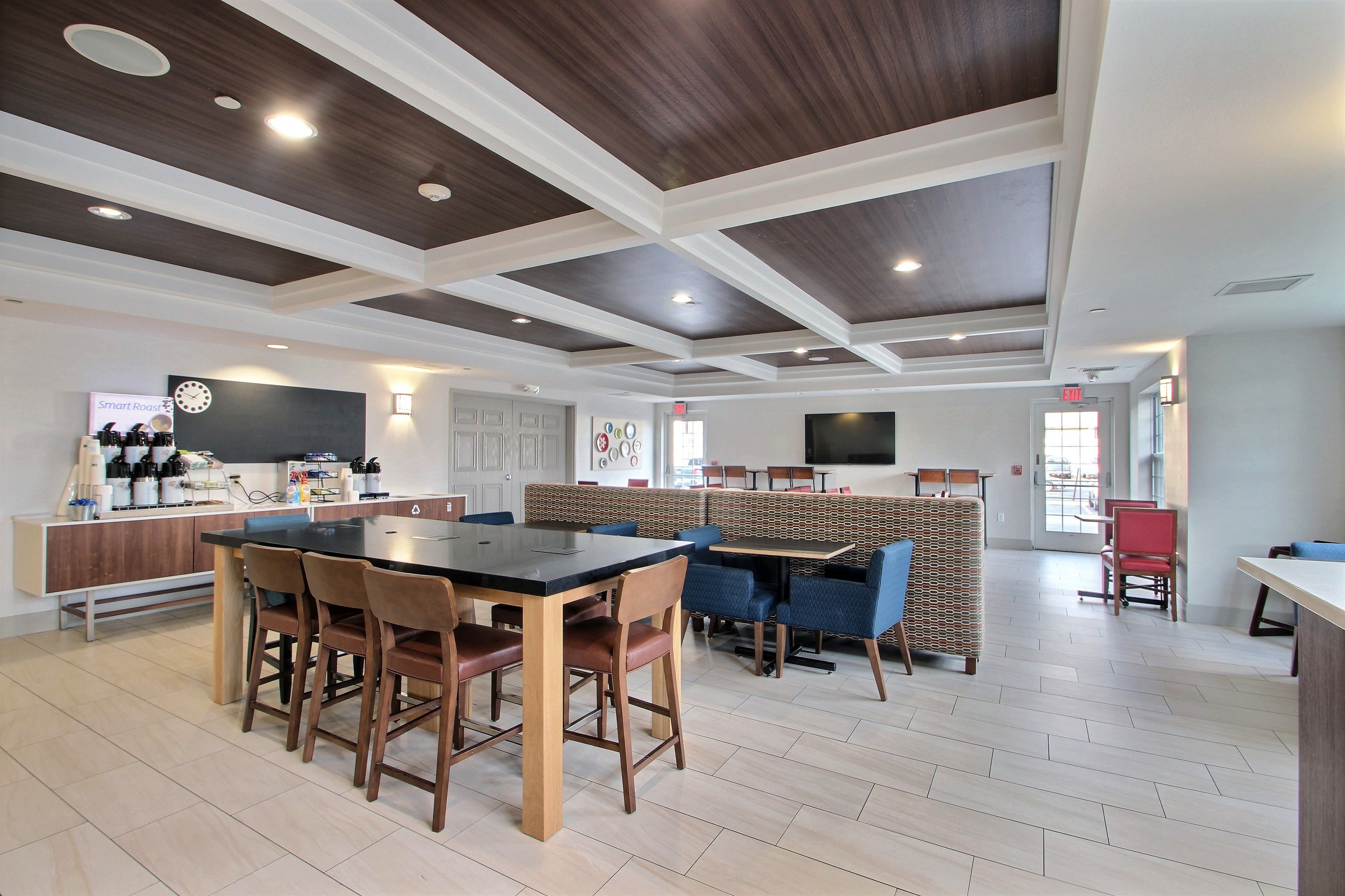 A modern dining area with a central table, surrounding chairs, and a counter with kitchen appliances.
