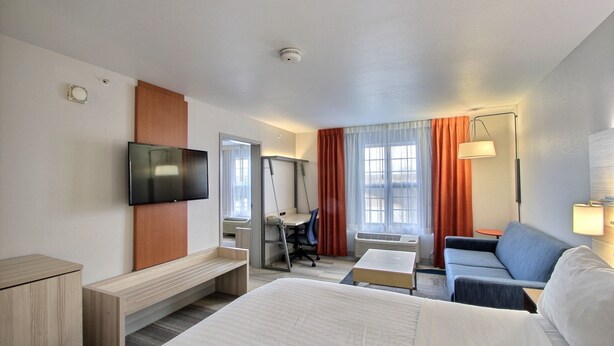 Habitación de hotel con cama, escritorio, silla, televisión, sofá y lámpara.