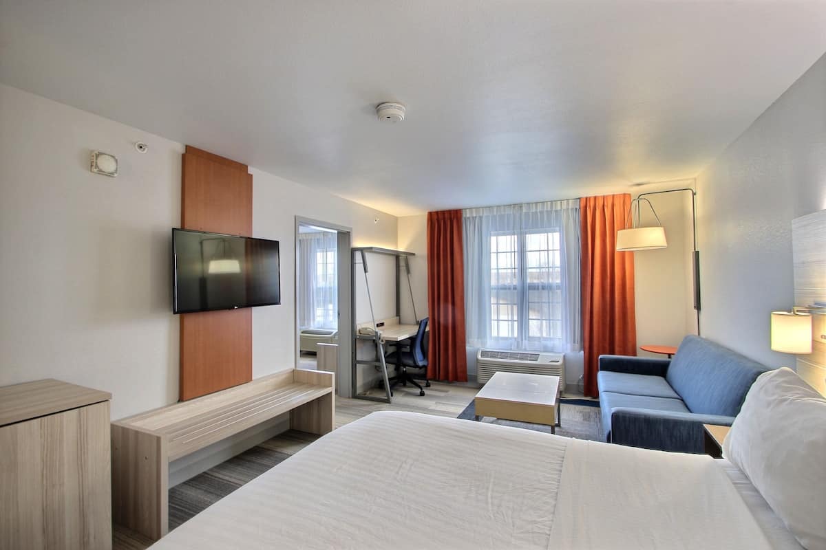 Ein Hotelzimmer mit Bett, Schreibtisch, Stuhl, Fernseher, Sofa und Lampe.
